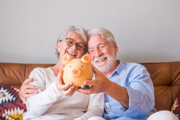 Close up of senior couple showing piggy bank to save money. Elderly couple holding piggy bank for investment and future planning concept. Happy retired couple holding piggy bank together at home