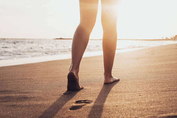 Пляжные путешествия - женщина, идущая по песчаному пляжу, оставляя следы на песке. Детали крупным планом женских ног и золотой песок на пляже Тенерифе. 