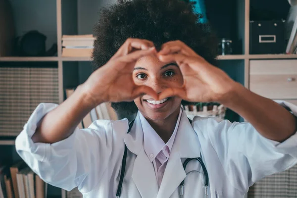 Woman doing heart shape gesture with hands. Smiling black female doctor making a love symbol using her hands. Healthcare worker expressing love and support to patients