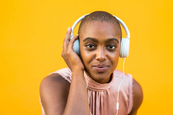 stock image Portrait of dark skinned woman listening to music on headphones over yellow background. Smiling african american lady enjoying her favorite song using wired audio equipment. Technology and entertainment  