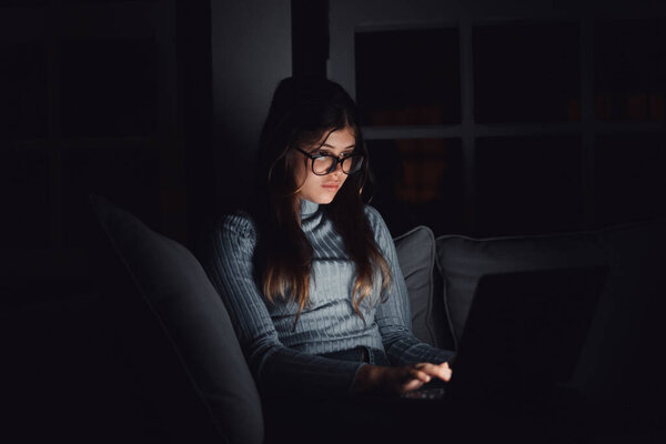 One happy and insomniac your woman using laptop late at night in the living room on the sofa at home chatting. Online girl surfing the net revising social media. Bored teenager using technology and internet.  