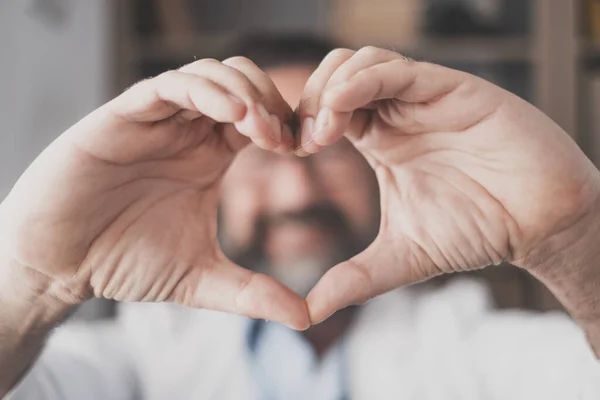 Man doing heart shape gesture with hands. Hand of male doctor making a love symbol. Healthcare worker expressing love and support to patients. Medical caregiver promoting charity donation