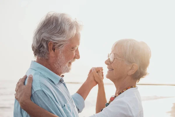 Couple of old mature people dancing together and having fun on the sand at the beach enjoying and living the moment. Portrait of seniors in love looking each others having fun.