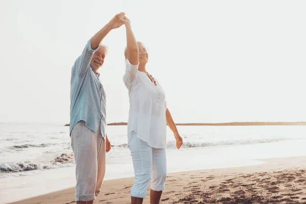 Couple of old mature people dancing together and having fun on the sand at the beach enjoying and living the moment. Portrait of seniors in love looking each others having fun.