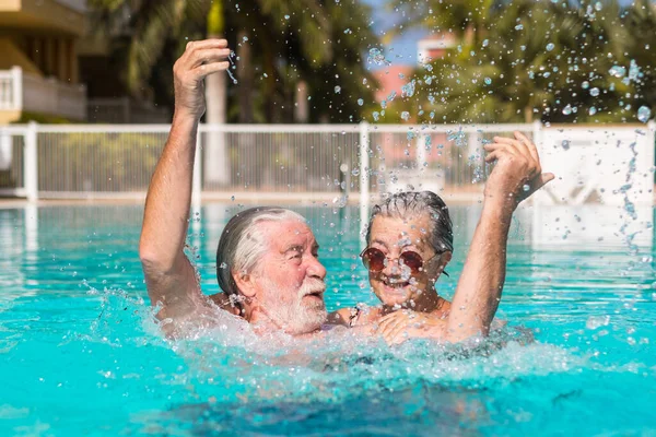 stock image Couple of two happy seniors having fun and enjoying together in the swimming pool smiling and playing. Happy people enjoying summer outdoor in the water 