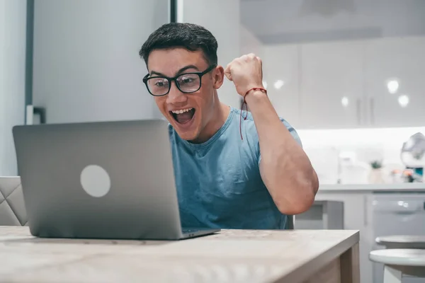 One young man working and winning something with laptop at home. Happy and euphoric teenager celebrating good news and having fun enjoying.