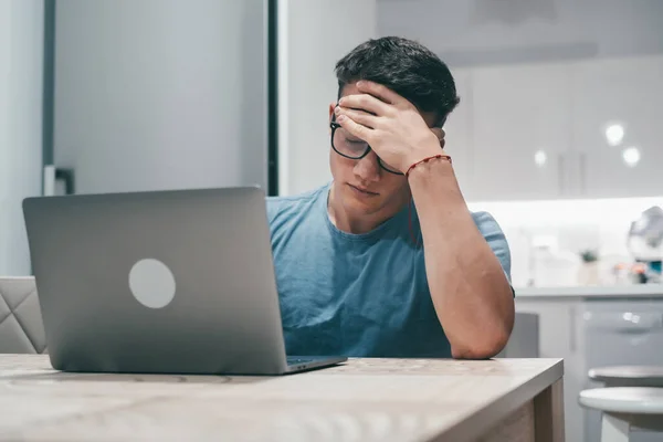 stock image Sick young man feeling unhealthy at home working with laptop on the table alone. Teenager boy touching his head after tired day. Overwork concept.