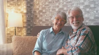 Sevimli ve güzel bir çift yaşlı insan gülümseyip kameraya bakıyor ve evde birlikte eğleniyorlar. Son sınıflar kanepede oturup eğleniyor ve dinleniyorlar..