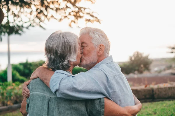 Head shot close up portrait happy grey haired middle aged woman snuggling to smiling older husband, enjoying tender moment at park. Bonding loving old family couple embracing, looking sunset.