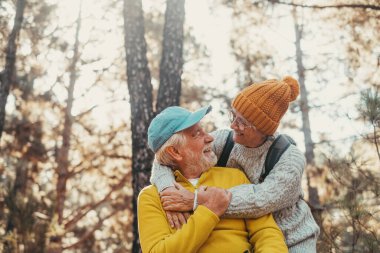 Head shot portrait close up of old people smiling and enjoying looking each other in the forest of mountain. Cute couple of mature seniors in love feeling happy and taking care.