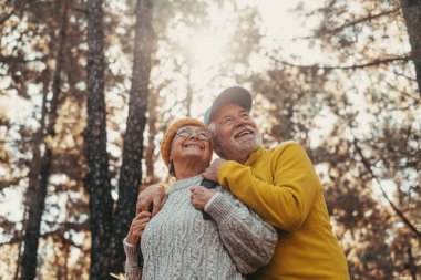 Head shot portrait close up of middle age cheerful people smiling and looking at the the trees of the forest around them. Active couple of old seniors hiking and walking together in the mountain having fun.