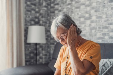 Head shot home portrait senior feeling bad indoor sitting on sofa, touches cheek suffering from sudden tooth pain feels unhealthy unhappy need dental service help, medical insurance concept