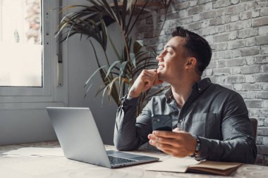 Kendine güveni tam bir adam bilgisayarındaki elektronik belgelerle işe ara verip telefonlara cevap veriyor. Gülümseyen genç serbest çalışan ev bilgisayarı ve akıllı telefon arasındaki verileri senkronize eder