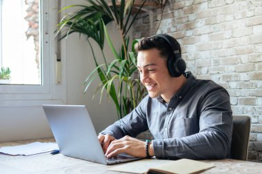 Happy businessman wearing headphones singing song at workplace, funny employee or freelancer using laptop, enjoying favorite track, listening to music, dancing, having fun during break
