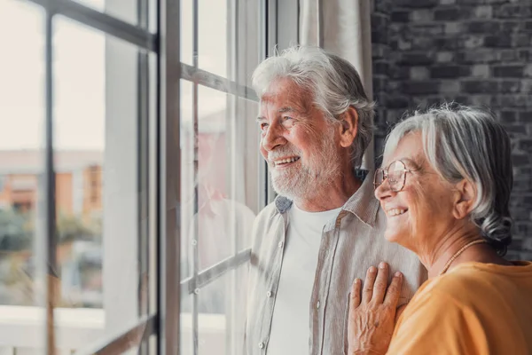 窓の近くに立って 遠くを見て 良い思い出を覚えているか 共通の未来を計画し 家で一緒に平和的な瞬間を楽しんでいる中年の高齢者の退職したカップルを愛する幸せな結合 — ストック写真