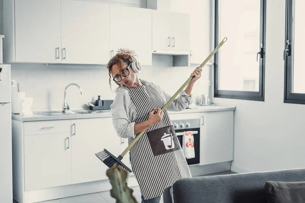 Carefree happy young woman cleaning house living room have fun dancing with mop, smiling overjoyed millennial girl feel excited enjoy making home chores sing entertain using floor broom or Swiffer