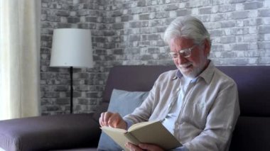 Yaşlı adamın evdeki kanepede kitap okuduğu görüntüler.