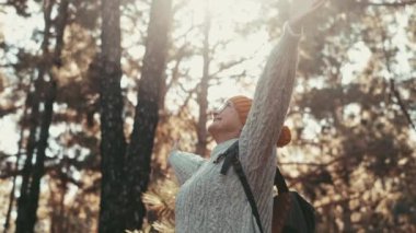 Güz aylarında güzel ormanda rahatlayan kazaklı ve yün şapkalı yaşlı bir kadının görüntüleri.