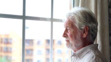 Evdeki pencerenin önünde yaşlı bir adamın görüntüsü.