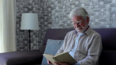 Yaşlı adamın evdeki kanepede kitap okuduğu görüntüler.