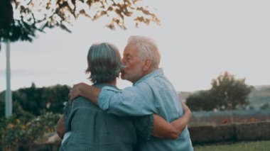Gün batımında parkta kucaklaşan romantik yaşlı çiftin görüntüleri.