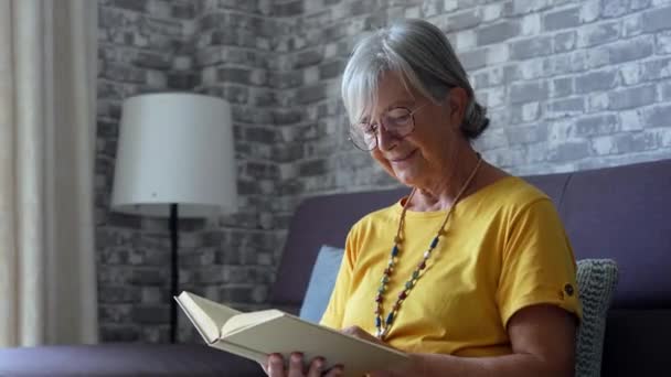 自宅のソファで本を読んでいる先輩女性の映像 — ストック動画