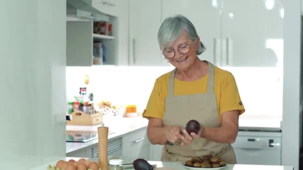家庭のキッチンでアボカドをスライスする先輩女性の映像 — ストック動画