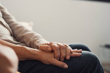 Yaşlı, sevecen bir kadının, olgun bir kocanın buruşuk ellerini kapaması, evde sevgi ve destek göstermesi. Şefkatli orta yaşlı bir çift samimi ve güvenilir bir sohbetin tadını çıkarıyor..