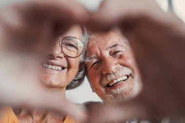 Yakın portre mutlu orta yaşlı aile samimi orta yaşlı çift parmakları ile kalp jesti, sevgi göstermek ya da kapalı alanda samimi duygular göstermek, kameraya bakarak.