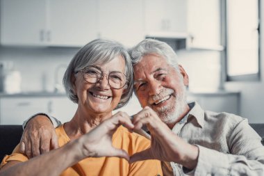 Yakın portre mutlu orta yaşlı aile samimi orta yaşlı çift parmakları ile kalp jesti, sevgi göstermek ya da kapalı alanda samimi duygular göstermek, kameraya bakarak.