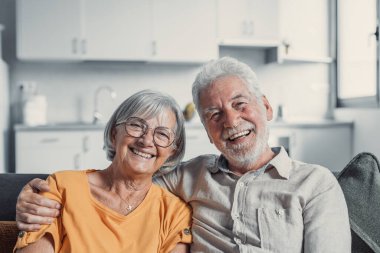 Gülümseyen 60 'lı yaşların portresi. Kanepede oturup sarılıyor, mutlu yaşlı çifti kucaklıyor. Oturma odasında dinleniyor.