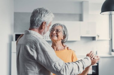 Neşeli aktif yaşlı emekli romantik çift oturma odasında gülerek dans, mutlu orta yaşlı karısı ve yaşlı koca evde eğlenmek, gülümseyen yaşlı aile dedesi birlikte bağ rahatlatıcı