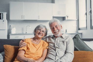 Gülümseyen 60 'lı yaşların portresi. Kanepede oturup sarılıyor, mutlu yaşlı çifti kucaklıyor. Oturma odasında dinleniyor.
