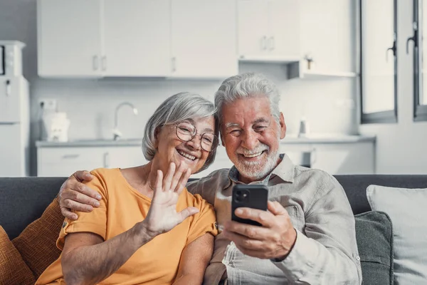 stock image Happy retired family couple using mobile phone for video call together, talking to relations, getting good news, having fun, smiling and laughing. Carefree mature pensioners chatting online on cell