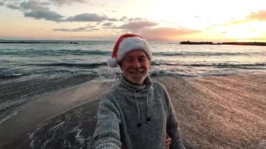 Gün batımında, Noel Baba şapkalı iki mutlu ve aktif yaşlının ya da emeklinin Noel 'i plajda kutlarken çekilmiş görüntüleri.