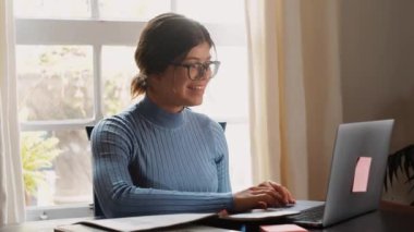 Evde dizüstü bilgisayarla çalışan kendine güvenen genç iş kadınının görüntüleri.