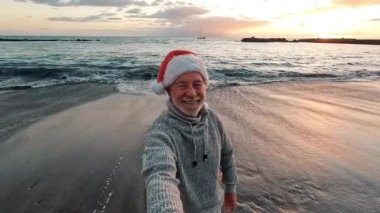 Gün batımında, Noel Baba şapkalı iki mutlu ve aktif yaşlının ya da emeklinin Noel 'i plajda kutlarken çekilmiş görüntüleri.