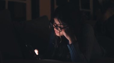 Evdeki kanepede akıllı telefon kullanan güzel bir genç kadının görüntüsü.