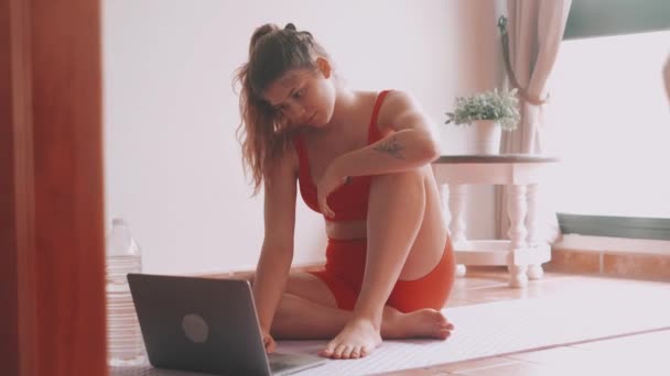 在家里客厅里用笔记本电脑练习瑜伽的漂亮年轻女人的镜头 — 图库视频影像