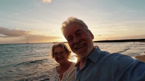 海と笑顔で夕日を楽しみ楽しむ2人の幸せと活動的な高齢者や年金受給者の映像 屋外で一緒に休暇を楽しむ高齢者 — ストック動画