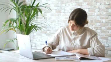 Evde dizüstü bilgisayarla çalışan kendine güvenen genç iş kadınının görüntüleri.