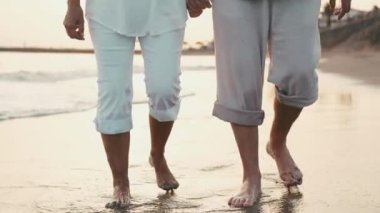 Gün batımında sahilde çıplak ayakla yürüyen romantik bir çiftin kırpılmış görüntüleri.