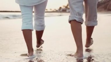 Gün batımında sahilde çıplak ayakla yürüyen romantik bir çiftin kırpılmış görüntüleri.