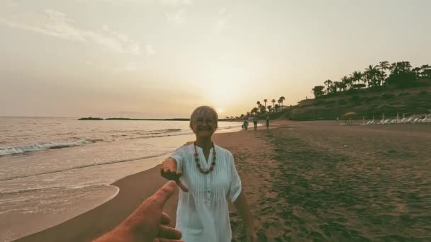 Zdjęcia Szczęśliwej Seniorki Trzymającej Swojego Mężczyznę Rękę Plaży Podczas Zachodu — Wideo stockowe