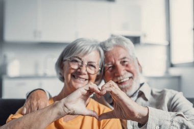 Yakın portre mutlu orta yaşlı aile samimi orta yaşlı çift parmakları ile kalp jesti, sevgi göstermek ya da kapalı alanda samimi duygular göstermek, kameraya bakarak.