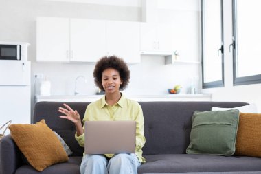 Kolay öğrenme. Gülümseyen genç melez bayan, dizüstü bilgisayarla kanepe arama bilgilerini izleyip video dersi alıyor. Pozitif siyah kadın el sallama becerilerini geliştirmek için çevrimiçi eğitim hizmetini kullanıyor