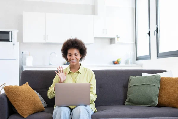 stock image Easy learning. Smiling young mixed race lady sit on couch search information using laptop watch webinar video lesson. Positive black woman use online education service to improve skills waving