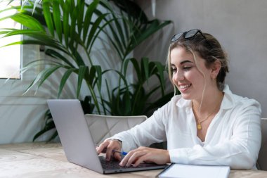 Evde bilgisayarla çalışan mutlu ve serbest bir genç kadın. Çevrimiçi öğrenim gören çekici iş kadını, dizüstü bilgisayar, web sörfü bilgileri veya internet mağazasından alışveriş yapıyor..