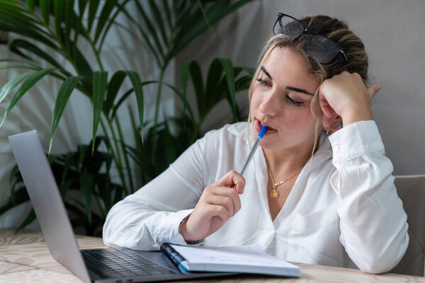 Portrait of serious millennial caucasian female student sit at desk at home study online on laptop. Thoughtful young attractive woman use computer take distant course or training. Education concept.
