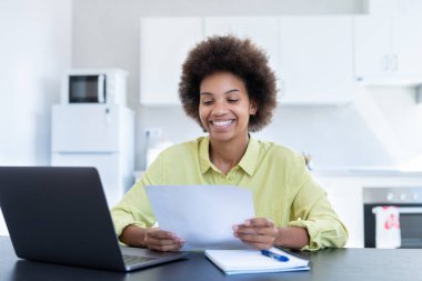 Mutlu gülümseyen, çalışan, uzaktan kumandalı genç zenci kadın şirket ofisinden proje raporu onayı için posta alıyor. Bin yıllık Afro-Amerikan çalışanın kağıt dökümanından iyi haberler okumasına sevindim.